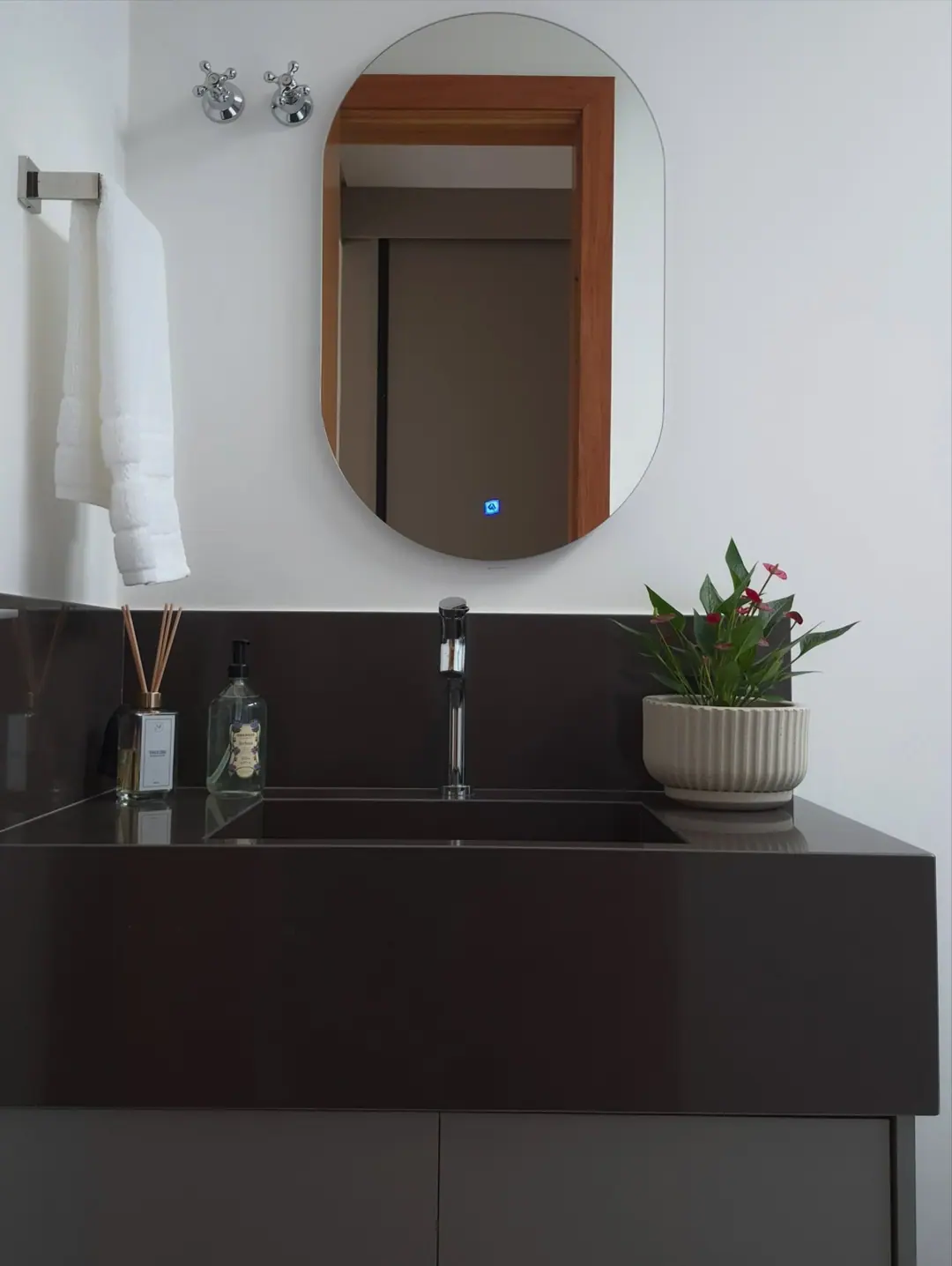 Lavabo com bancada e cuba em quartzo de tom profundo e espelho oval iluminado