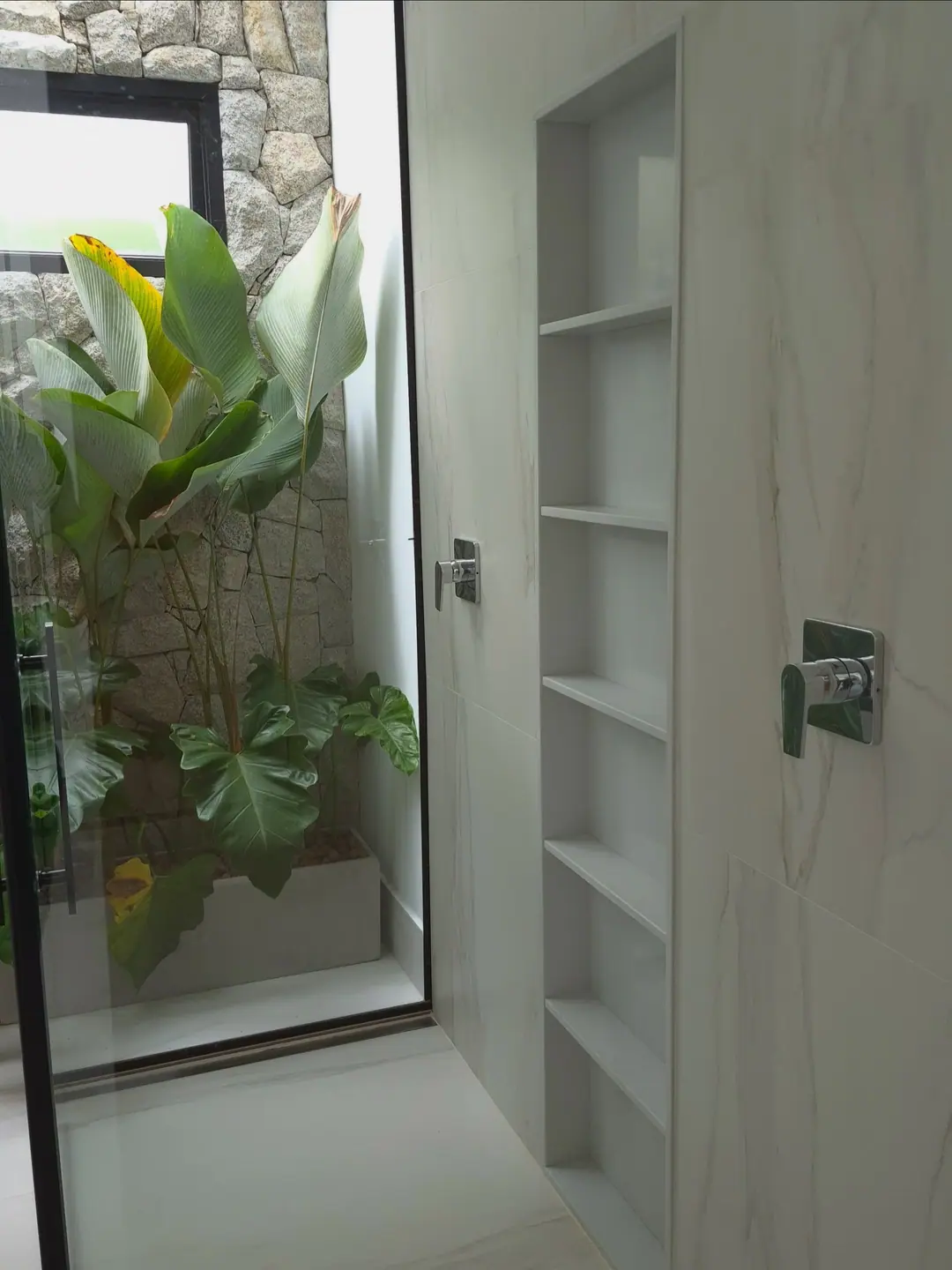 Nichos verticais em quartzo branco dentro do box, com jardim ao fundo